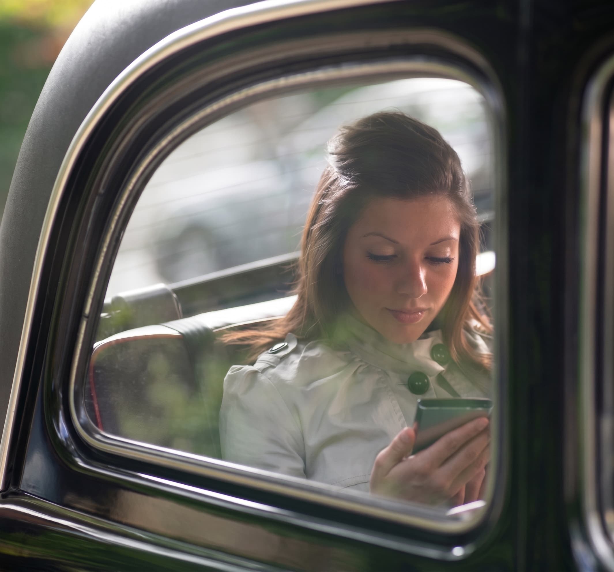 A young woman in the back seat of a car, reading a message on her phone.